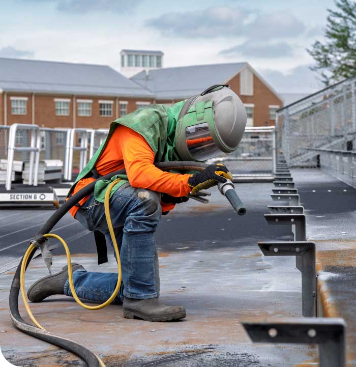 Worker sandblasting a steel beam on an elevated walkway